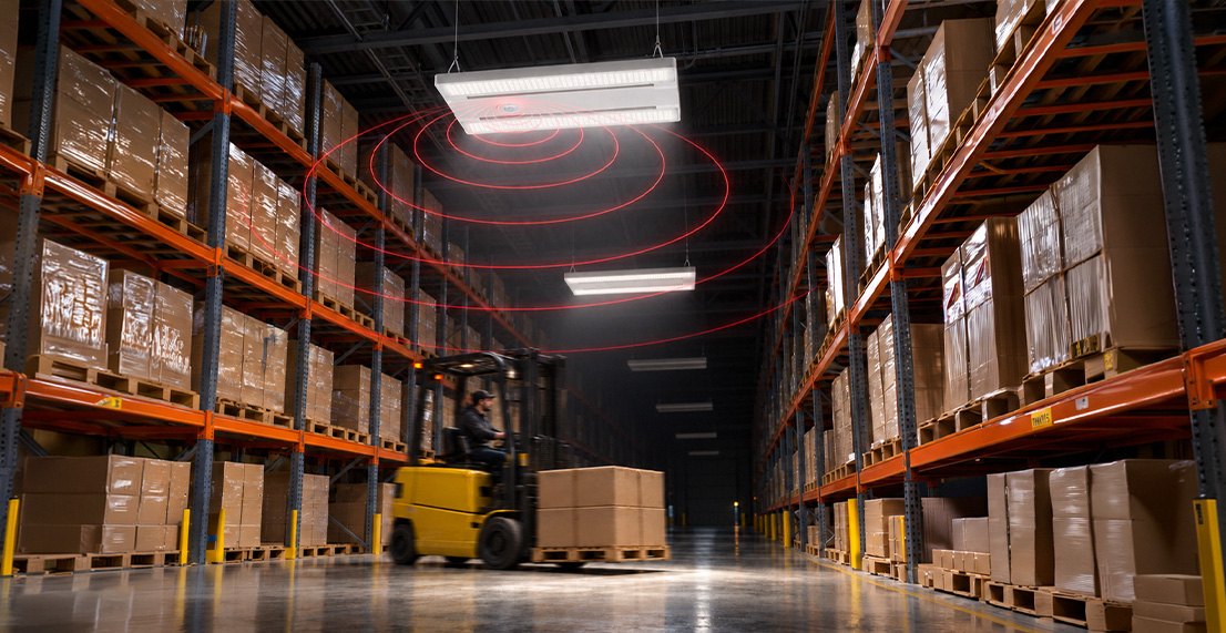 Warehouse aisle lit by linear LED high bays, with sensor detection rings drawn below one fixture