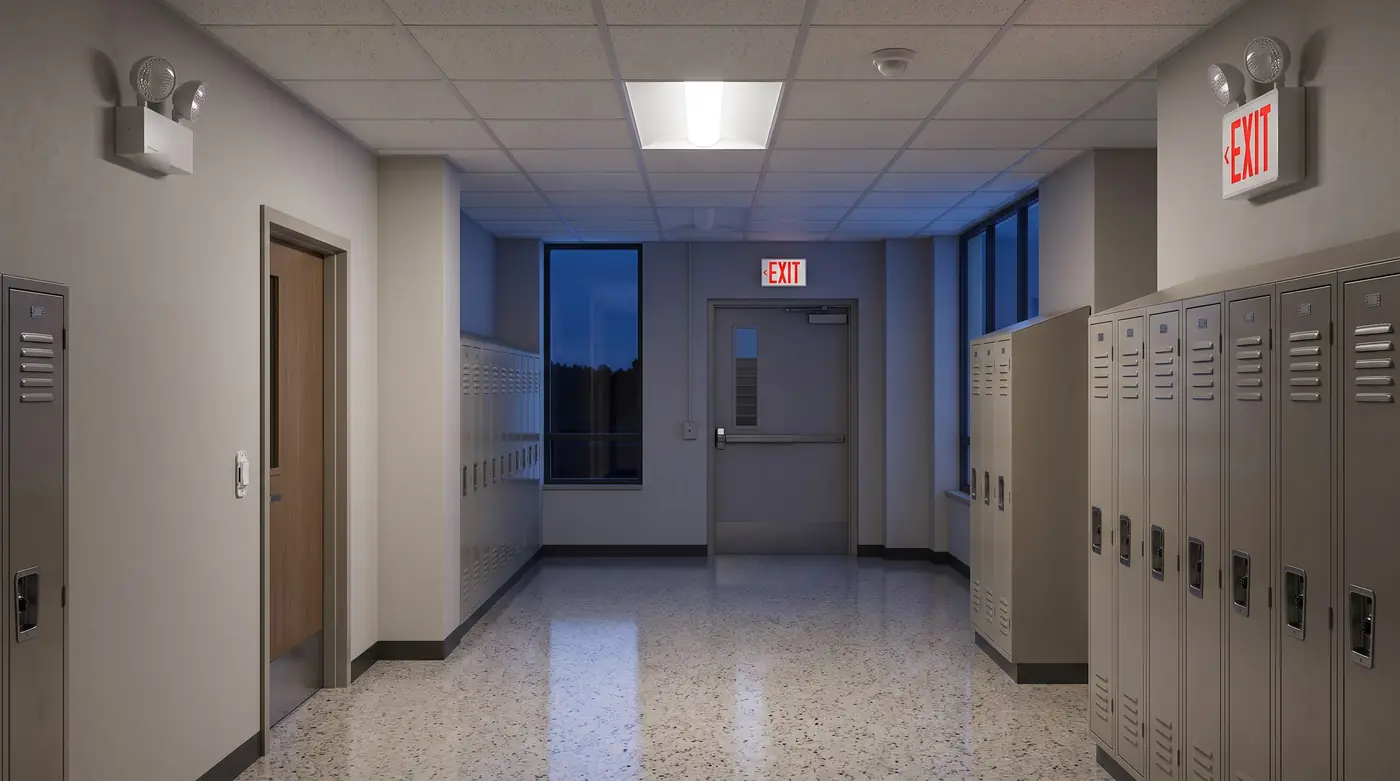 A school corridor with an exit sign over the stair door, a combo unit, a two-head emergency light, a ceiling sensor beside a troffer and a wall switch